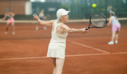 Wall Mural - Two elderly women doubles playing against young women in tennis on court