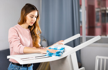 Young european woman cleaning up the apartment wipes a chair with a damp cloth