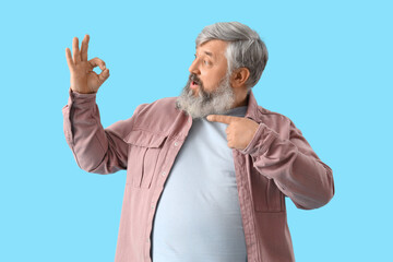 Mature bearded man pointing at OK gesture on blue background