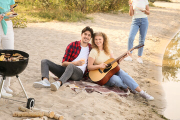 Wall Mural - Young couple with drink and guitar on beach at barbeque party