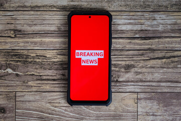 top view of breaking news text in phone over wooden table