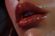 © EliteStock - Close-up of a young woman's glossy lips, reflecting light with a soft sheen, highlighting her delicate features and captivating smile.