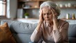 © Suchithra - Elderly woman with Headache. Managing Stress. An elderly woman sitting on a sofa, holding her head in pain