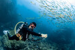 © zephyr_p - Male scuba diver swimming with a school of fish at Richelieu Rock, one of the popular dive sites of Andaman sea. Scuba diving experience in Thailand. Underwater world concept