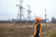 © Melena-Nsk - A man in a protective orange helmet and vest inspects power transmission line supports. Late autumn, bad weather