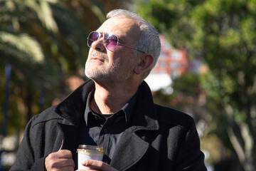 Mature man in coat drinking takeaway in park in autumn