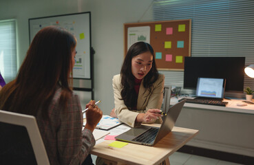 Financial accounting concepts Two businesswomen, confident freelancers working in finance and calculations Discuss management, analysis, and document guidelines on the office board.