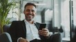 © Lion - Businessman smiling while sitting in a chair, holding a phone and reading news in a modern office. Minimalistic background focusing on his positive expression.