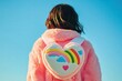 © Running opossum - Back view of a young kidult woman wearing a pink fluffy jacket and heart-shaped backpack with a rainbow design under a blue sky