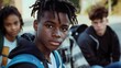 © James - Serious black teenage student wearing blue backpack in close-up portrait with diverse classmates blurred in background, copy space