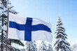 © mlphoto - A Finnish flag flutters in the wind, set against a backdrop of snow-covered pine trees under a clear blue sky