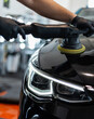 © alones - Professional man with polishing tool polishing black car in detailing garage. Car care and scratch removal