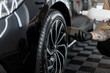 © alones - A man with a sponge blackens the tires of a car in a garage. Car wash and detailing studio