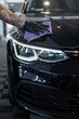 © alones - A man wipes a black car dry with a cloth. Detailing. Car care and washing