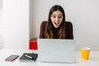 © Xavier Lorenzo - Front view of excited young woman reading good news on laptop sitting on table at home