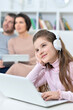 © aletia2011 - Cheerful little girl using a laptop at home with her parents in the background.
