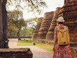 Young female tourist in dress exploring historic park of Ayutthaya, Thailand. Surrounded by ancient temples and statues, she enjoys peaceful atmosphere and rich cultural heritage. view from the back