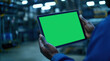 © Саша Федюк - An industrial worker is shown using a tablet with a green mock-up screen in a factory environment.