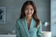 © Surachetsh - An Asian woman in a pastel green suit smiles warmly at the camera, her confident stance highlighted by the cool, grey-green studio background.