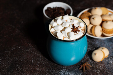 Wall Mural - blue mug of spicy hot chocolate with marshmallows on dark background, closeup top view