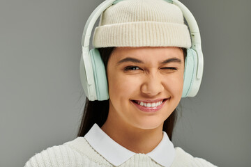 A young woman with an infectious smile expresses joy while wearing trendy headphones and a hat.