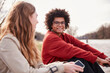 © MACO - Young mixed race guy and European girl sitting outside along a river hanging out. Munich, Germany
