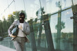 © Milos - This image portrays a masked person in a business suit, urgently running with a green bag against a backdrop of glass architecture, highlighting mystery and agility.