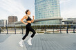 © BGStock72 - A determined woman jogs confidently in modern urban surroundings, showcasing her fitness journey against a sleek architectural backdrop