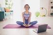 © deagreez - Young woman in activewear practicing yoga at home on a sunny day with laptop nearby for virtual class