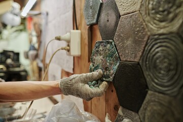 Recycling factory worker in gloves putting molded reused plastic tiles on wall while creating new sustainable products