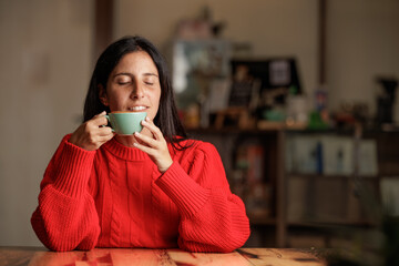 Portrait of a beautiful smiling lady enjoying the aroma of specialty coffee and drinking cappuccino from a cup while resting in the restaurant. Portrait, close up.
