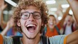 © Lens Legacy - A young, curly-haired man wearing glasses and a backpack is shown joyfully smiling and cheering in a vibrant crowd, capturing a moment of pure excitement and happiness.