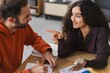 © Studio Marmellata - A woman with curly hair points while speaking to a male colleague in a casual workspace, creating a lively and engaged interaction that suggests active communication and teamwork.