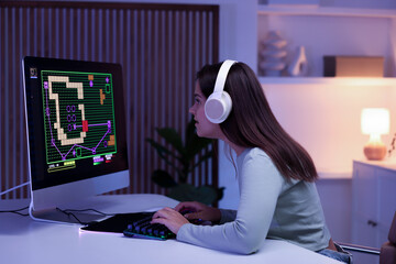 Wall Mural - Woman in headphones playing video game with keyboard at table indoors