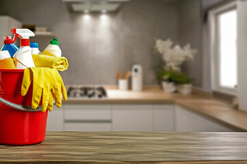 Bucket with cleaning items on wooden table and blurry modern kitchen background. Washing set colorful with copy space banner.