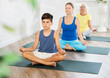 © JackF - Grandmother, mom and teen son do half lotus position of Ardha Padmasana Sidhasana with hands clasped in mudra of knowledge in gym. Family three generations keep fit with exercise. Healthy lifestyle