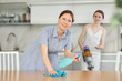 © JackF - Smiling mother cleansing the table using spray detergent, teen daughter vacuuming floor in the kitchen