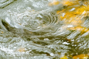 Poster - The photograph captures swirling water in dynamic motion, with hints of orange and green reflections adding depth and a sense of fluidity and nature's beauty.