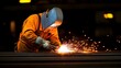 © maesarin - Welder wearing protective gear performing steel plate welding in a dark industrial workshop with only the bright sparks from the welding torch illuminating the area