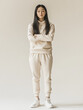 © Itsaya - full body shot of Asian woman wearing pale pastel colored tracksuit, standing confidently with arms crossed. soft background enhances her relaxed yet assertive demeanor