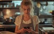 © tongpatong - While working in the restaurant kitchen, a young, blonde woman is utilising a mobile.