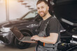 © anatoliycherkas - Mechanic man mechanic manager worker using a laptop computer checking car in workshop at auto car repair service center. Engineer young man looking at inspection vehicle details under car hood.