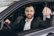 © anatoliycherkas - Cheerful bearded man holding key from auto, buying brand new car in showroom. Happy smiling guy buying new automobile, sitting inside car and showing automatic key at camera