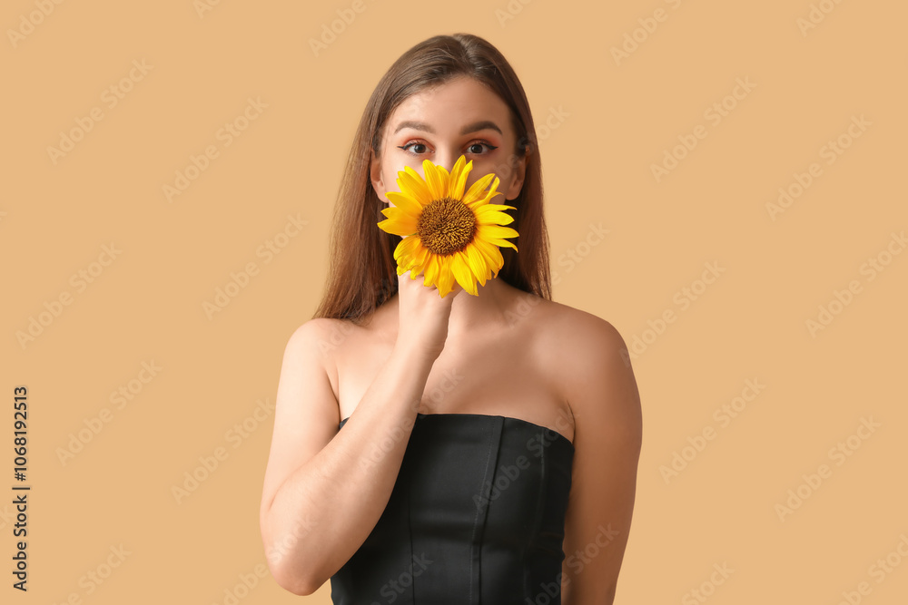 Young woman with beautiful sunflower on orange background