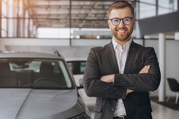 Wall Mural - Portrait of Modern car seller standing in car salon with arms crossed with copy space