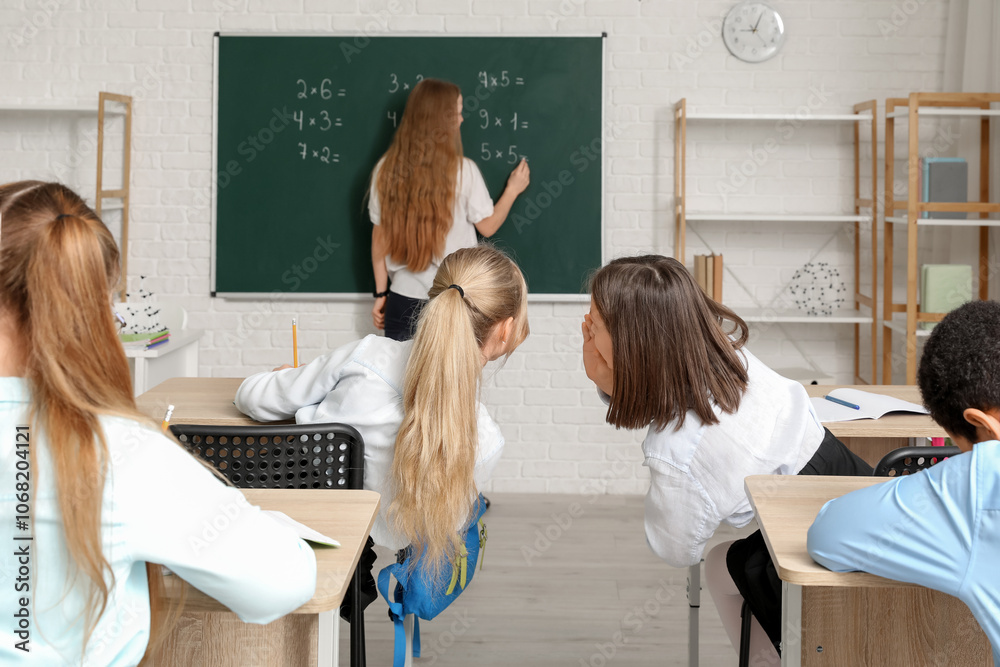 Little girls whispering behind teacher's back during lesson in classroom