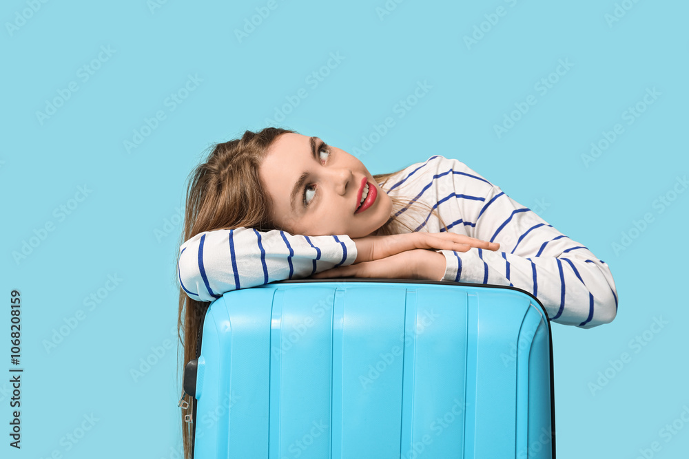 Beautiful young woman with blue suitcase on color background