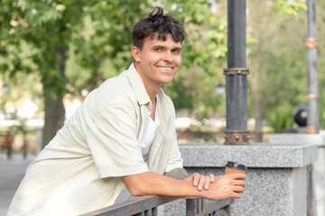 Poster - Handsome young man with cup of delicious latte leaning on railing outdoors