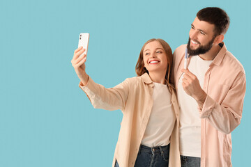 Wall Mural - Happy young couple with pregnancy test taking selfie on blue background