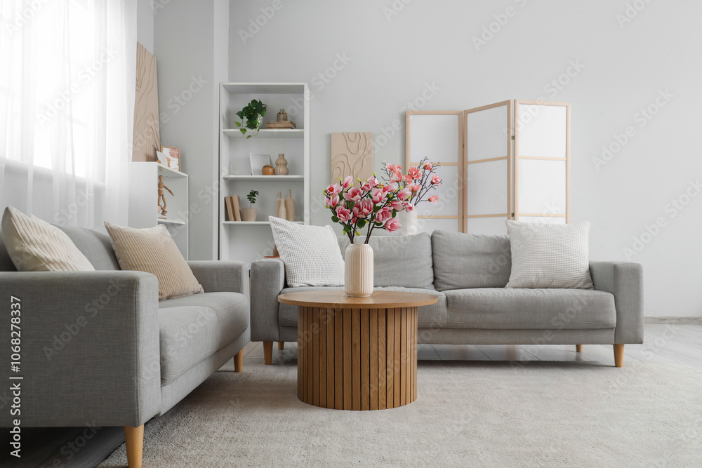 Cozy sofas and magnolia flowers in vase on coffee table in room